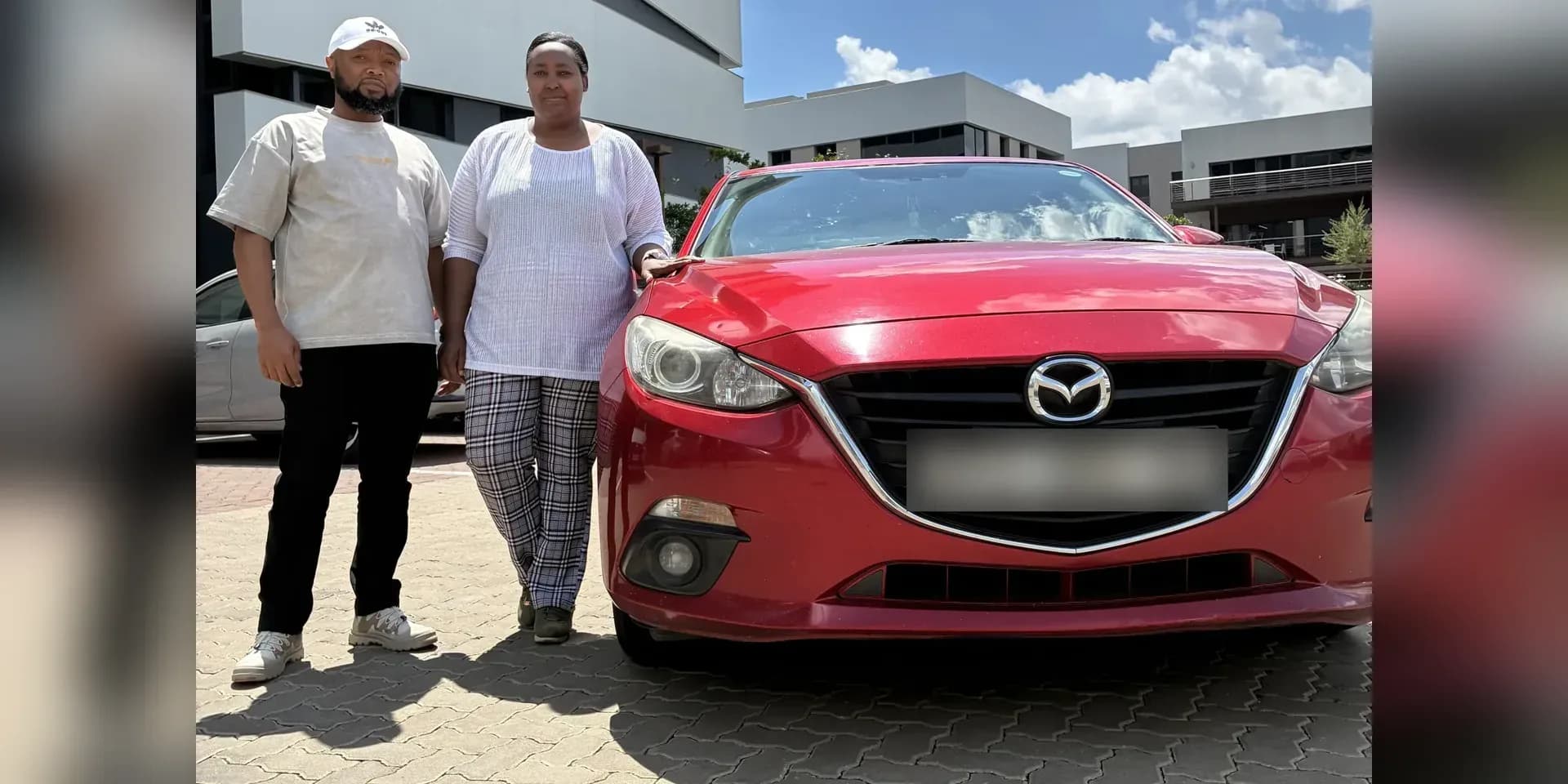 Ben Mlaza standing with a companion beside his red Mazda3 hatchback